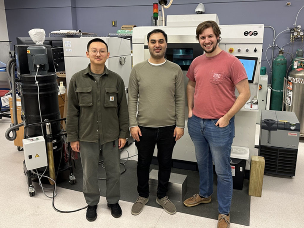 Three researchers stand side by side in front of a piece of heavy equipment in a lab.