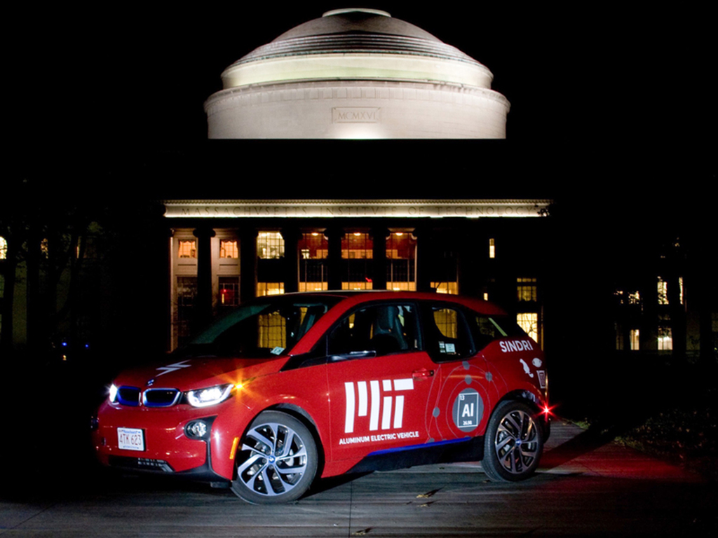 Red electric vehicle with MIT logo illuminated in front of the MIT dome