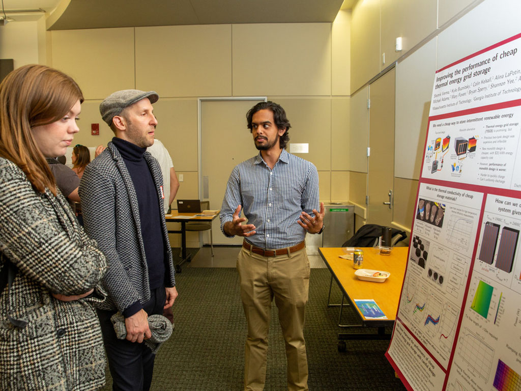 Shomik at his poster display explaining research to two people